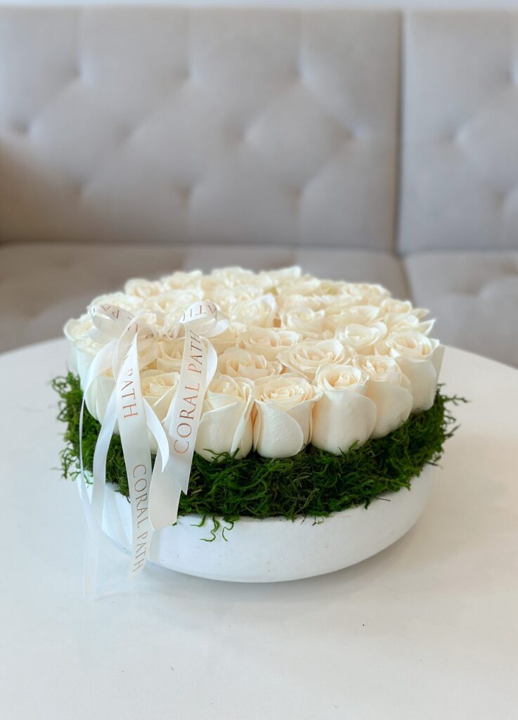 Low profile white ceramic bowl with white and ivory roses and preserved moss underneath the roses.