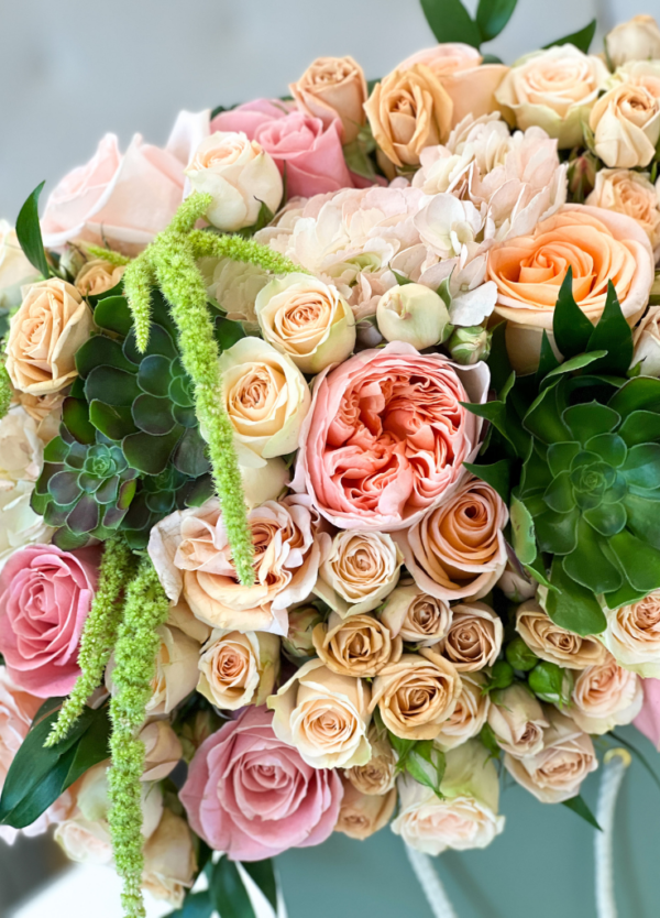 A beautiful bouquet of peach garden roses, succulents, amaranthus, and spray roses in a flower box close-up