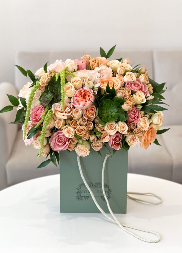 A beautiful bouquet of peach garden roses, succulents, amaranthus, and spray roses in a flower box.