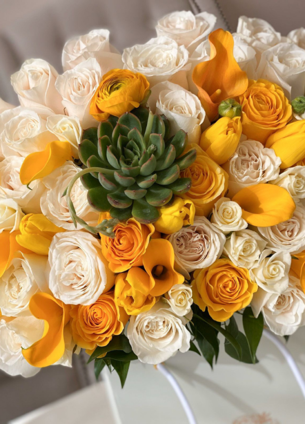 Mix of succulents, yellow tulips, yellow roses and spray roses, and yellow calla lilies arranged in a bag box.