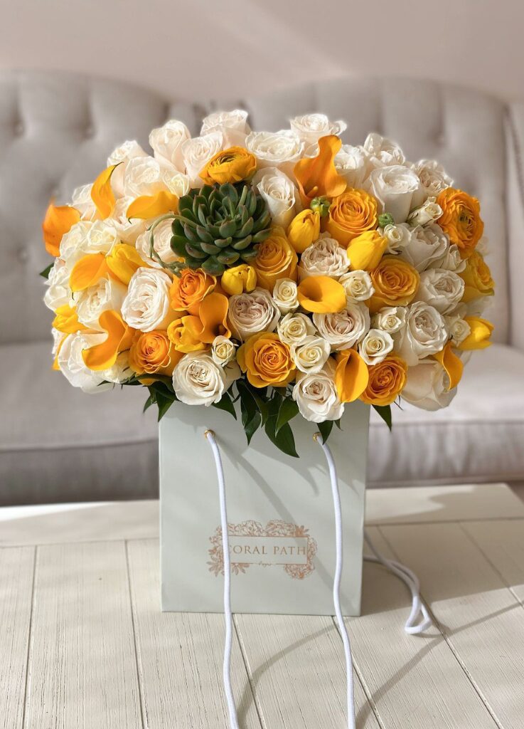Mix of succulents, yellow tulips, yellow roses and spray roses, and yellow calla lilies arranged in a bag box.