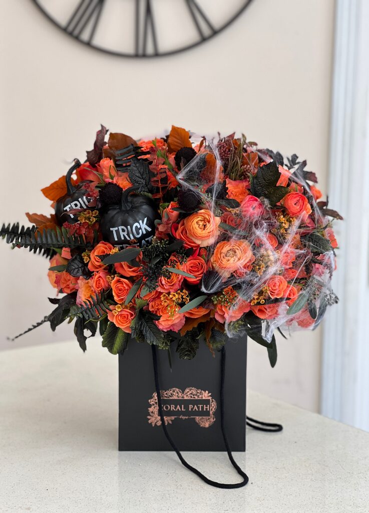 Flower bag featuring Halloween inspired flowers, orange roses, orange ranunculus, spider webs, and faux pumpkins.