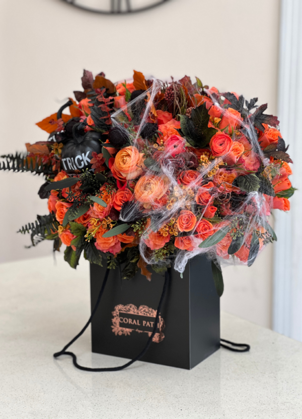 Flower bag featuring Halloween inspired flowers, orange roses, orange ranunculus, spider webs, and faux pumpkins.