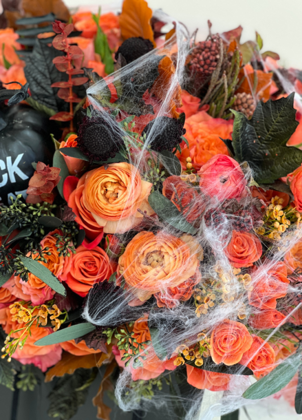 Flower bag featuring Halloween inspired flowers, orange roses, orange ranunculus, spider webs, and faux pumpkins.