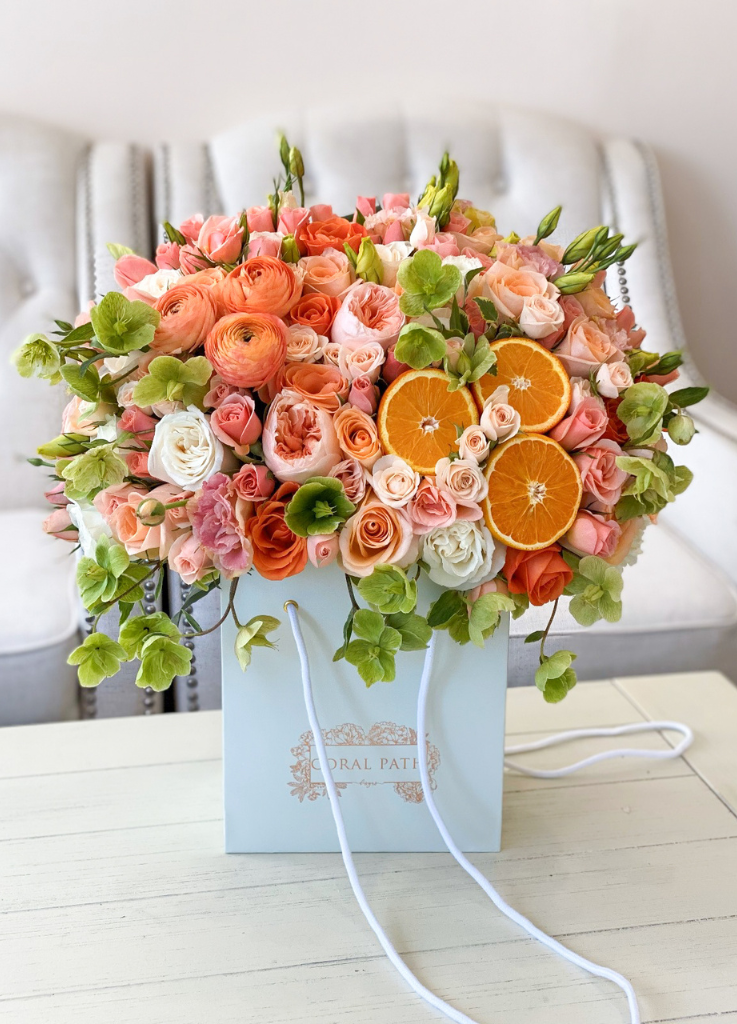 Flower arrangement in a bag, featuring garden roses, ranunculus, and real oranges.