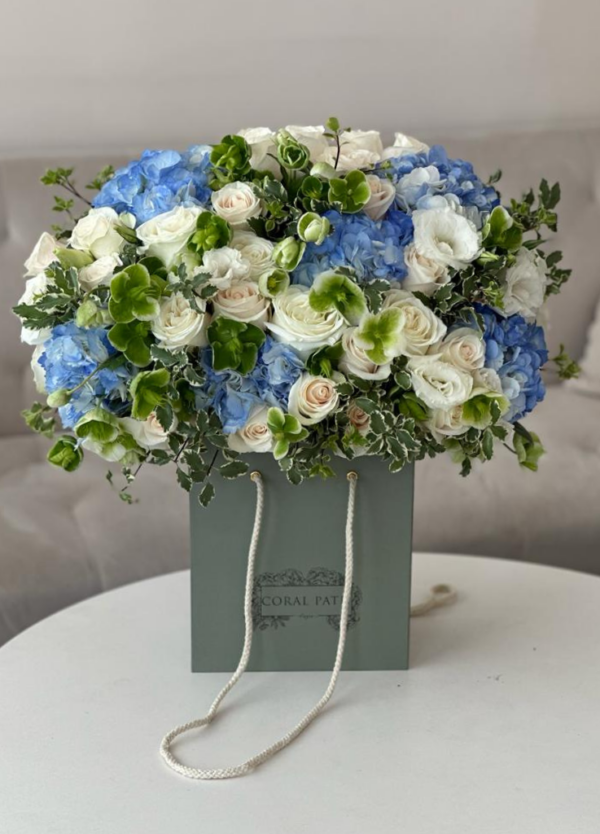 Blue hydrangea, hellebores, ivory roses and other fillers in a bag box.