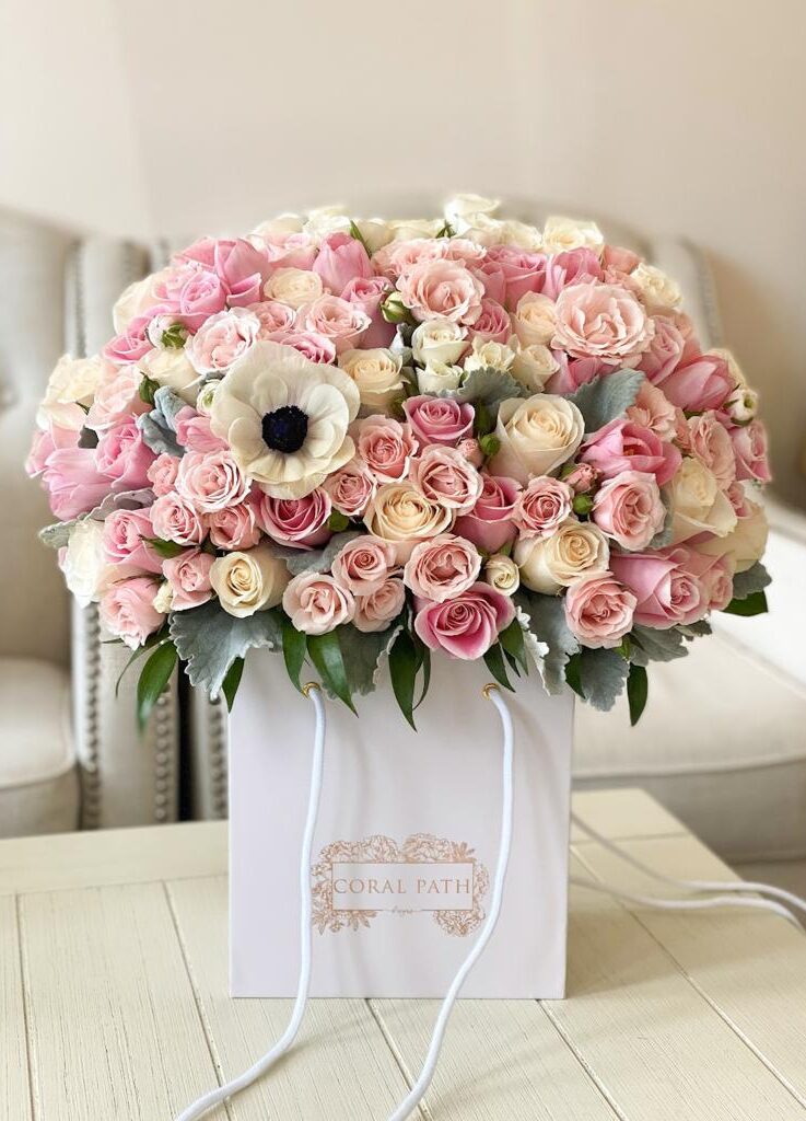 A dusty color blend of roses, anemones, duty miller leaves all arranged in a bag.