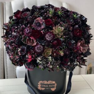 Dark burgundy and black flower mix arranged in a hat box with a logo.