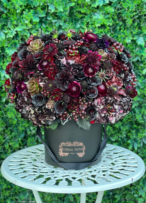 Dark burgundy and black flower mix arranged in a hat box with a logo.