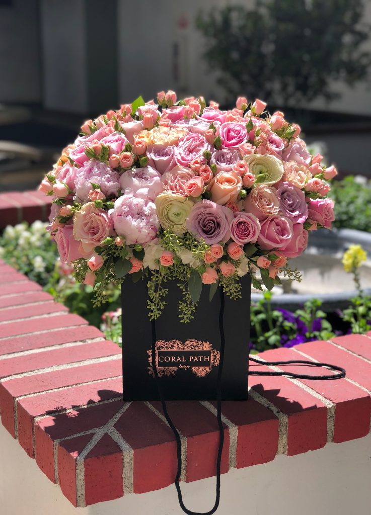 A flower arrangement in a bag with roses, peonies, eucalyptus and ranunculus. Pink and purple flowers.