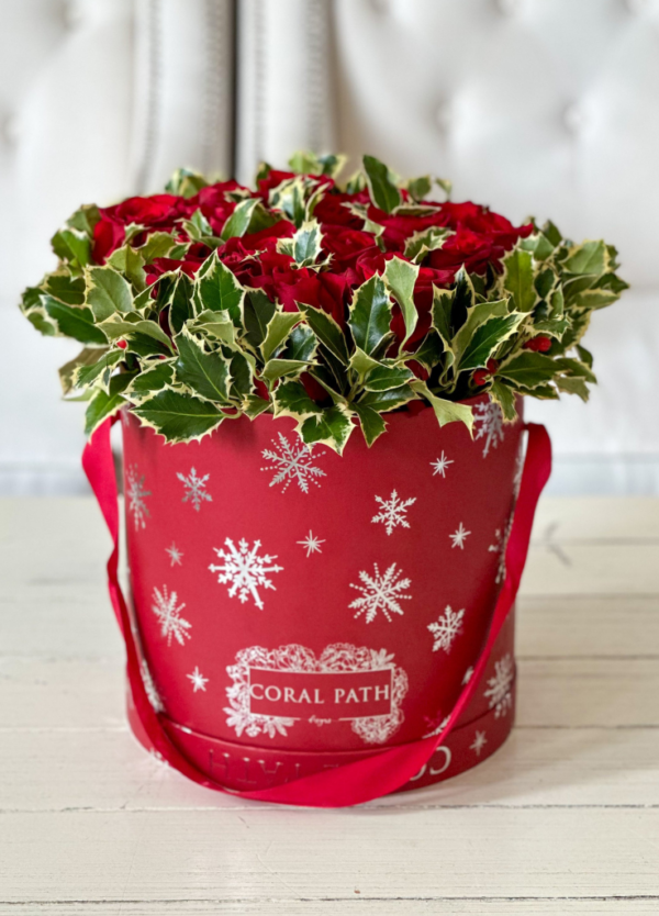 Image description: Roselyn version of 'Christmas Time is Here' arrangement with red roses, holly, and silver snowflakes in exclusive holiday boxes.