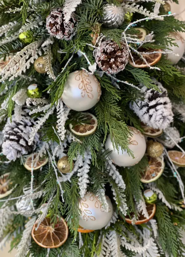 Festive Christmas Tree-shaped arrangement by Coral Path in a square box, featuring dried oranges, pine cones, faux snow, and ornaments.