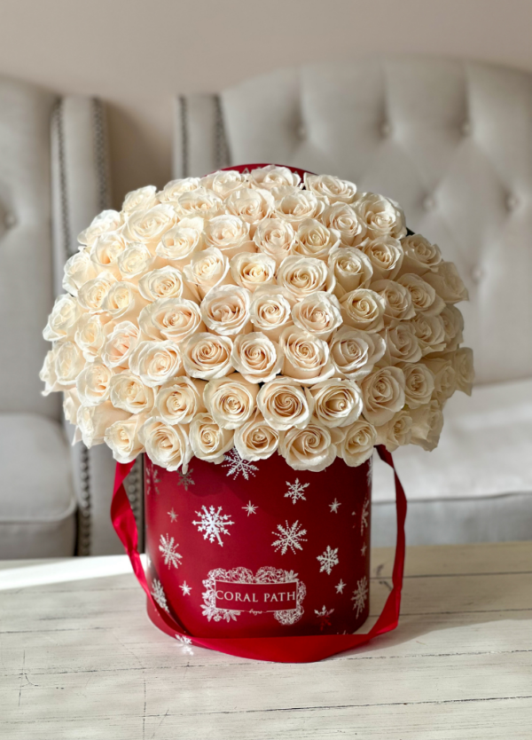 Image description: Ivory roses arranged in a floral hat box with shiny silver snowflakes embossed on the box.