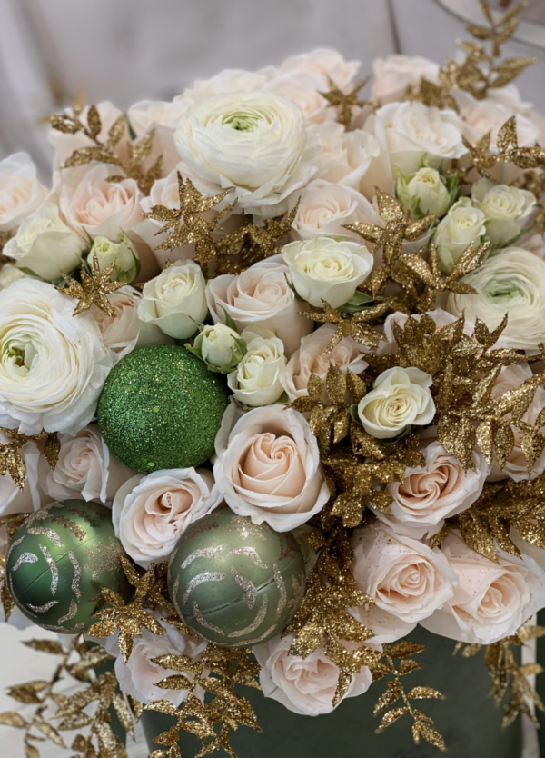 Image description: Holiday arrangement with white and ivory roses, green accents, and glittery gold fillers, creating a festive and joyful atmosphere.