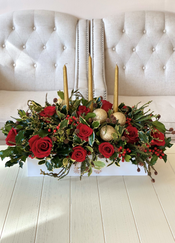 Rectangular box arrangement with red roses, real candles, holiday greenery, and Christmas ornaments, adding festive charm to any space.