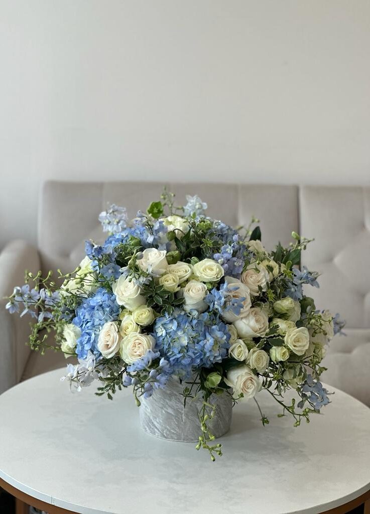 Blue hydrangea, hellebores, ivory roses and other fillers in a bag box.