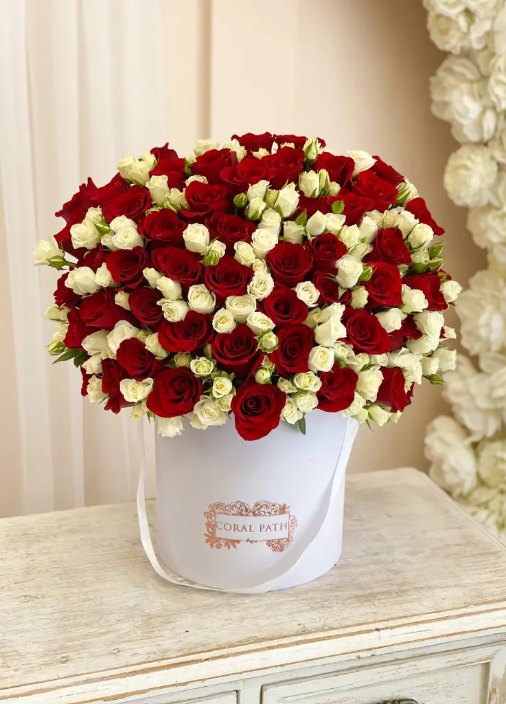 Red roses with white spray roses. Arranged in a hat box.