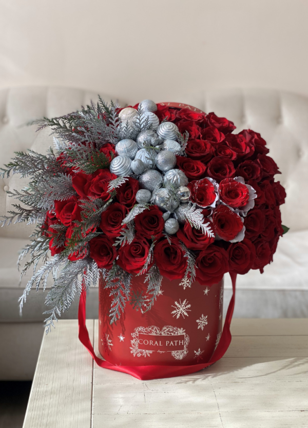 Image description: Exclusive Christmas-themed flower arrangement with red boxes, silver snowflakes, ornaments, and greens for festive holiday delivery.