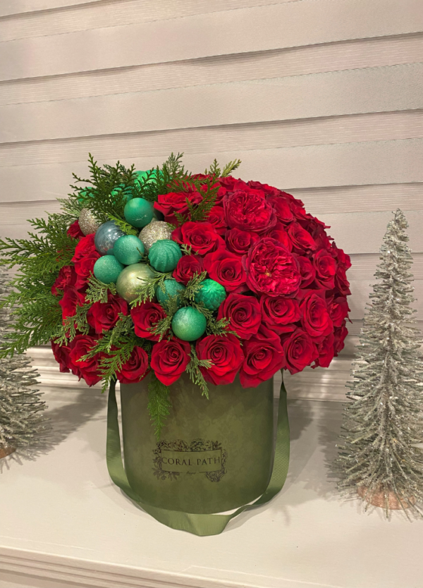 "Image description: Circular hat box arrangement in Victoria Green with red roses, Christmas ornaments, and fern leaves for festive elegance.