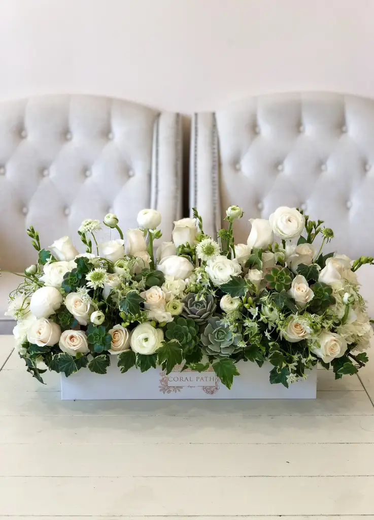 White ranunculus and garden roses arranged with greenery in a long rectangular box