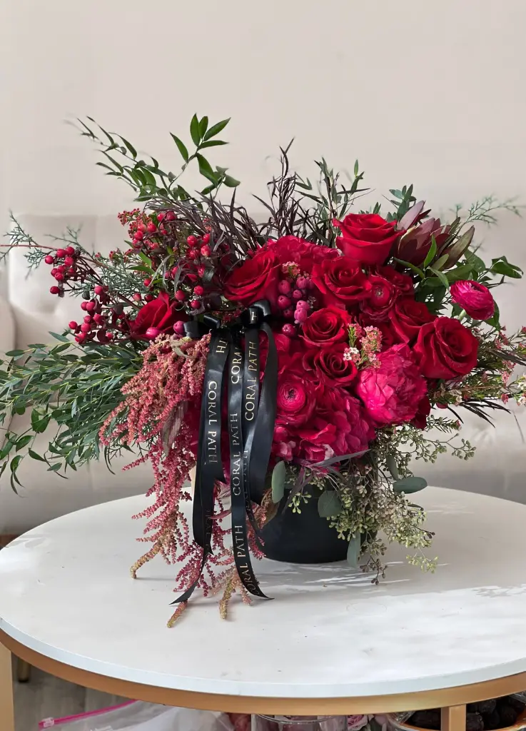 A wild arrangement look, with red roses, peonies, ilex berries, astilbe in a black vase.