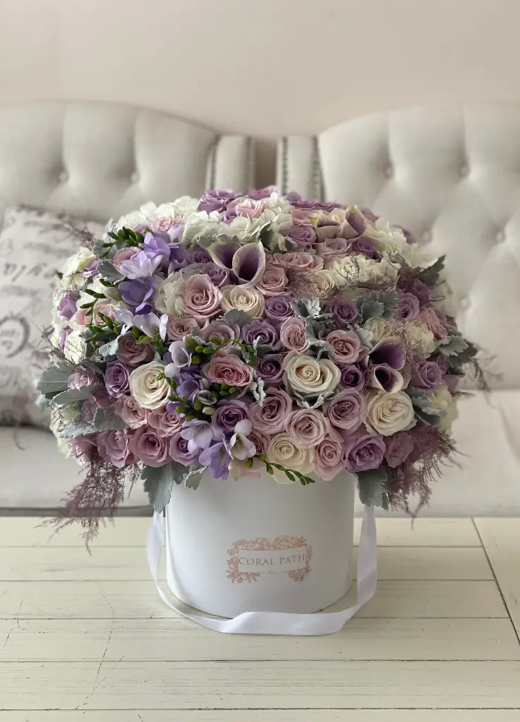 Lavender roses and calla lilies mixed with ivory roses and dusty miller in a white hat box.