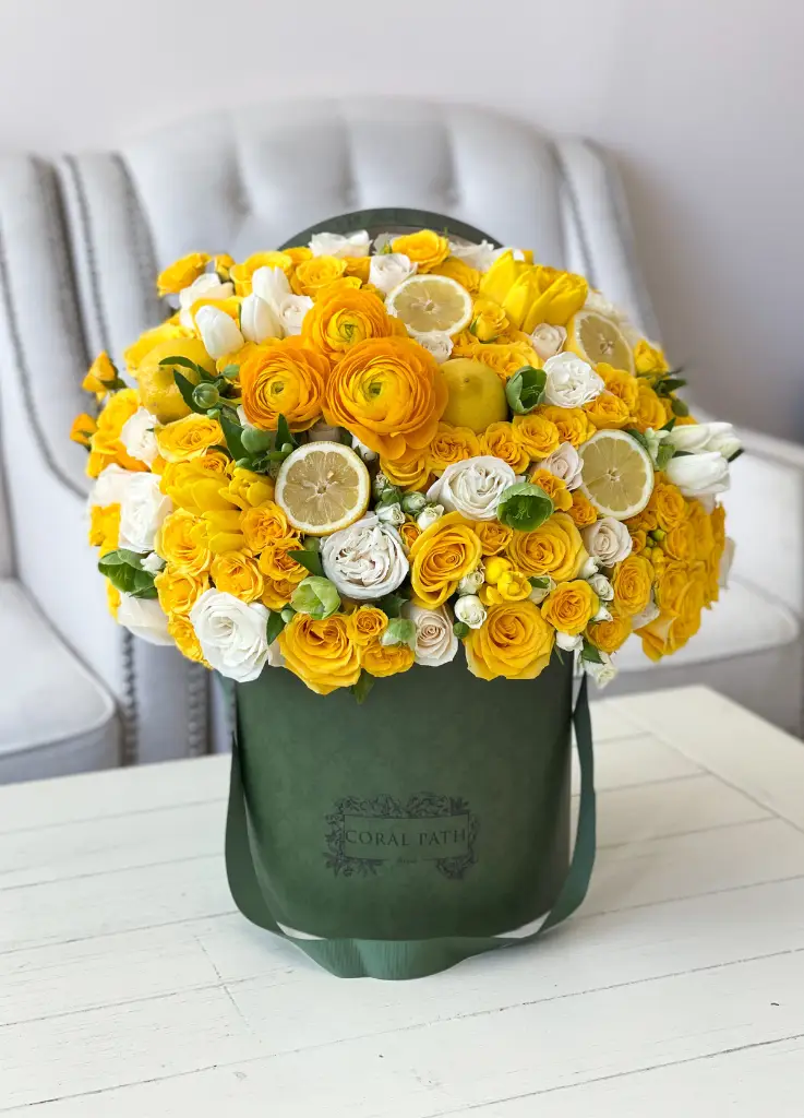 Yellow flowers and lemons mixed in a bouquet arranged in a green hat box.