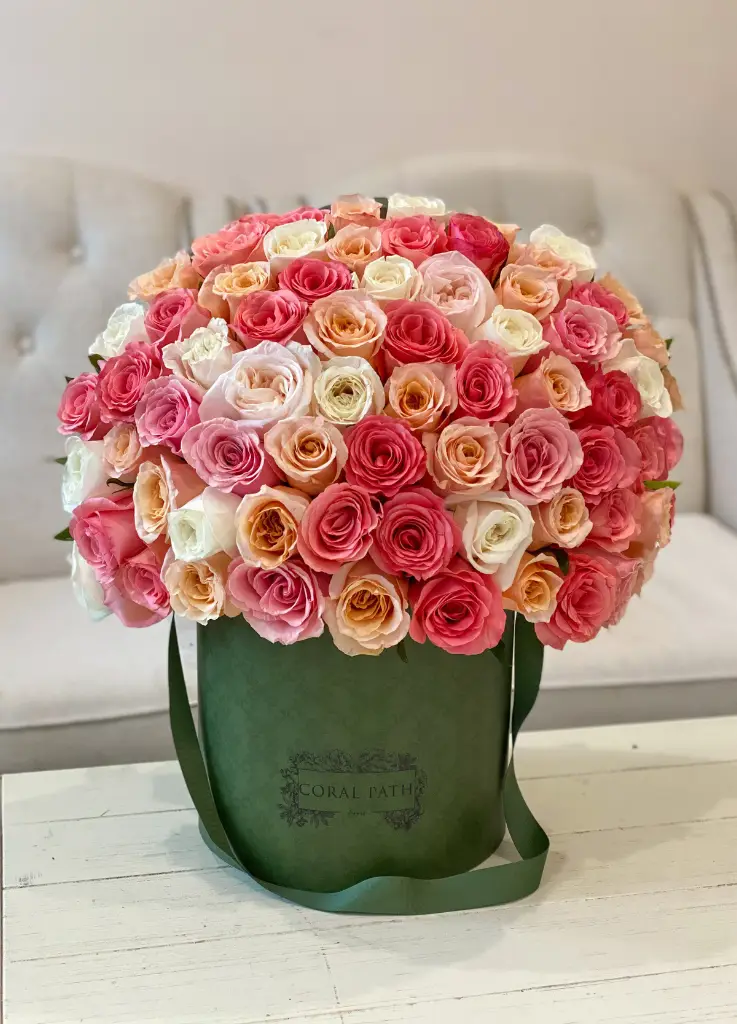 Coral, ivory, and peach roses arranged in a green hat box.