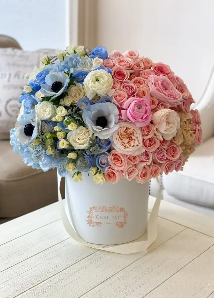 Blue and pink flowers arranged in a hat box. One side blue one side pink with anemones, roses and more