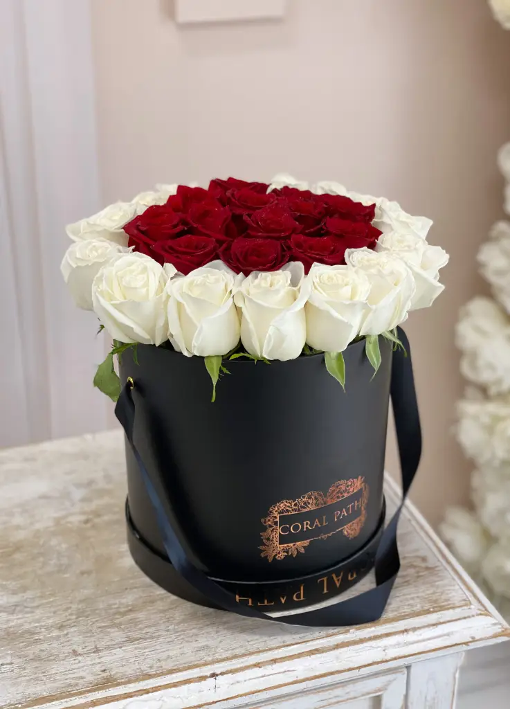 Red and white roses arranged in a black hat box.