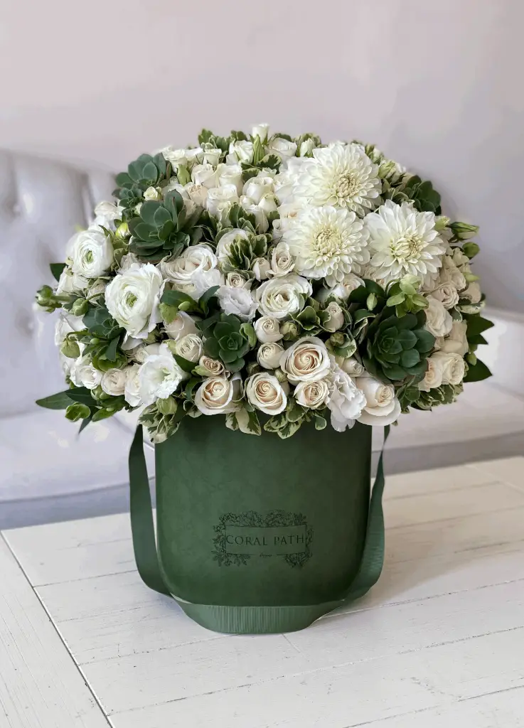 White flowers mixed with succulents in a green hat box.