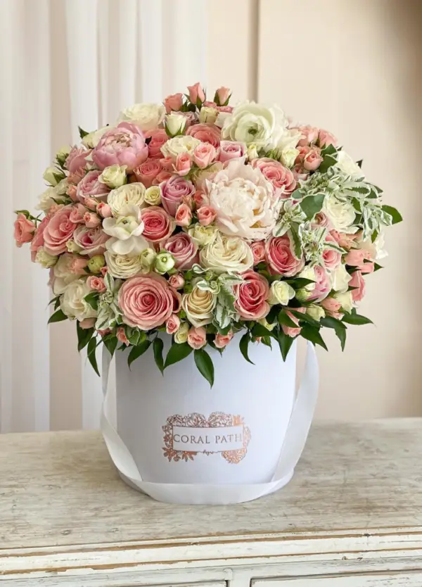Light pink and ivory roses mixed in with peonies and greenery all in a hat box.
