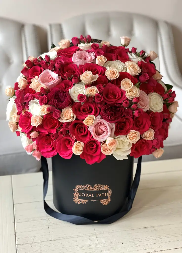 Mixed red, hot pink and white flowers in a black hat box.