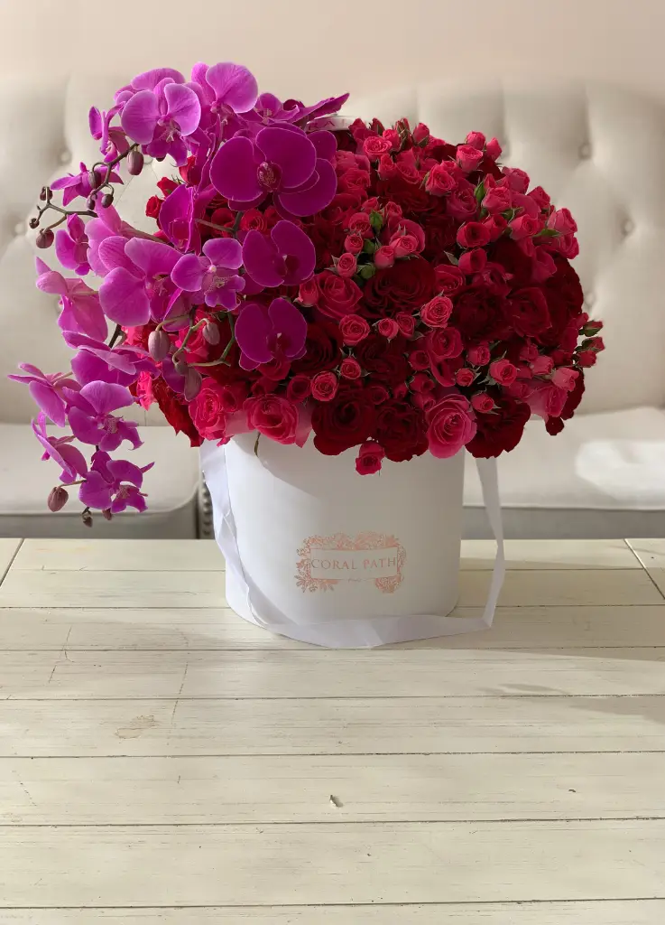 Bold and vibrant roses with violet orchids from the side all arranged in a hat box.