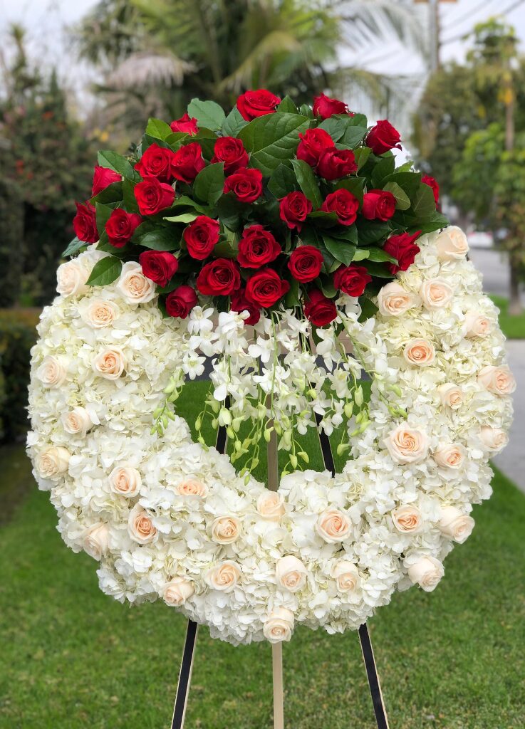 standing circle sympathy wreath with red roses on top and dendro orchids