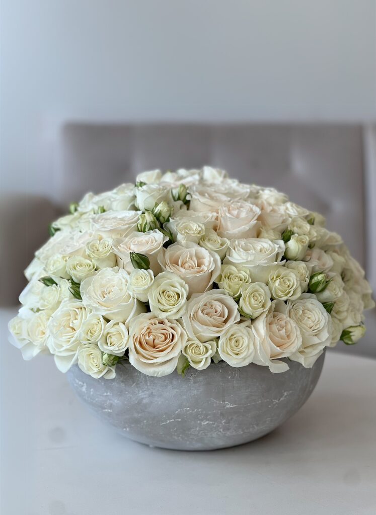 white roses arranged in a low concrete gray bowl
