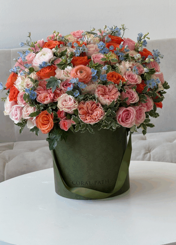 Elegant peach-toned flower arrangement featuring lush garden roses, ranunculus, and delphinium in a neutral ceramic vase, styled on a marble surface with soft natural lighting for a refined, luxury floral aesthetic.