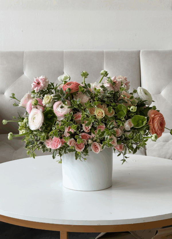 Blush garden rose and ranunculus arrangement with spray roses and green hellebore in a white vase, styled with airy seasonal greenery.