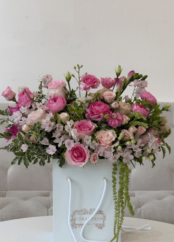 Pink garden rose and ranunculus arrangement in a white Coral Path hat box with cascading greenery and soft seasonal blooms.